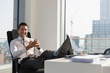 © Tom Merton/Caia Image - Portrait confident businessman using smart phone with feet up on desk in highrise office