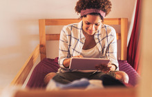 Young female college student using digital tablet on dorm room bunk bed