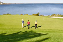 Male Golfers Walking Toward Pin On Sunny Lakeside Putting Green