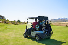 Male Golfers Driving Golf Cart On Sunny Golf Course Greens