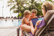 © Paul Bradbury/Caia Image - Mother and sons relaxing with digital tablet at poolside