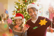 Portrait Smiling Father And Daughter In Santa Hats Holding String Of Paper Snowflakes