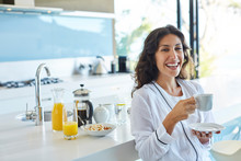 Portrait laughing woman in bathrobe drinking coffee in morning kitchen