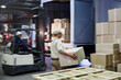© Ryan Lees/Caia Image - Workers and forklift loading cardboard boxes onto trucks at distribution warehouse loading dock