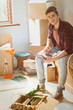 © Justin Pumfrey/Caia Image - Portrait smiling young man using laptop surrounded by moving boxes in new apartment