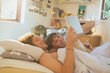 © Justin Pumfrey/Caia Image - Smiling young couple laying in bed using digital tablet