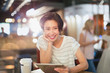 © Tom Merton/Caia Image - Portrait smiling young woman using digital tablet and drinking coffee in cafe