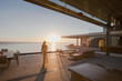 © Tom Merton/Caia Image - Woman walking on sunset modern, luxury home showcase exterior patio with ocean view