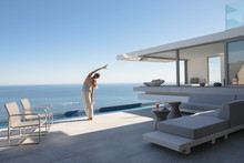 Woman Practicing Yoga Side Stretch On Modern, Luxury Home Showcase Exterior Patio With Sunny Ocean View