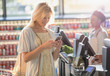© Tom Merton/Caia Image - Smiling young woman texting with cell phone at grocery store market checkout