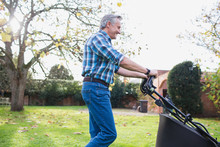 Senior Man Moving Lawn With Lawnmower In Autumn Backyard
