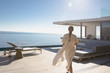 © Tom Merton/Caia Image - Woman walking on sunny modern, luxury home showcase exterior patio with ocean view