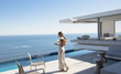 © Tom Merton/Caia Image - Woman walking and texting with smart phone on sunny modern, luxury home showcase patio with ocean view