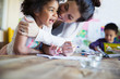 © Sam Edwards/Caia Image - Affectionate, happy mother hugging toddler daughter coloring at table