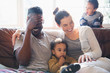 © Sam Edwards/Caia Image - Laughing, happy multi-ethnic family on living room sofa