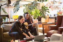 Young Man And Woman Recording Music, Playing Guitar And Keyboard Piano In Apartment