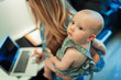 © Paul Bradbury/Caia Image - Mother working at laptop and holding cute baby daughter