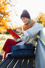 Young Woman Using Digital Tablet On Autumn Park Bench