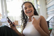 © Sam Edwards/Caia Image - Portrait happy young woman with smart phone and tea laughing