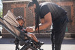 © Sam Edwards/Caia Image - Father fastening toddler son in stroller on sunny sidewalk