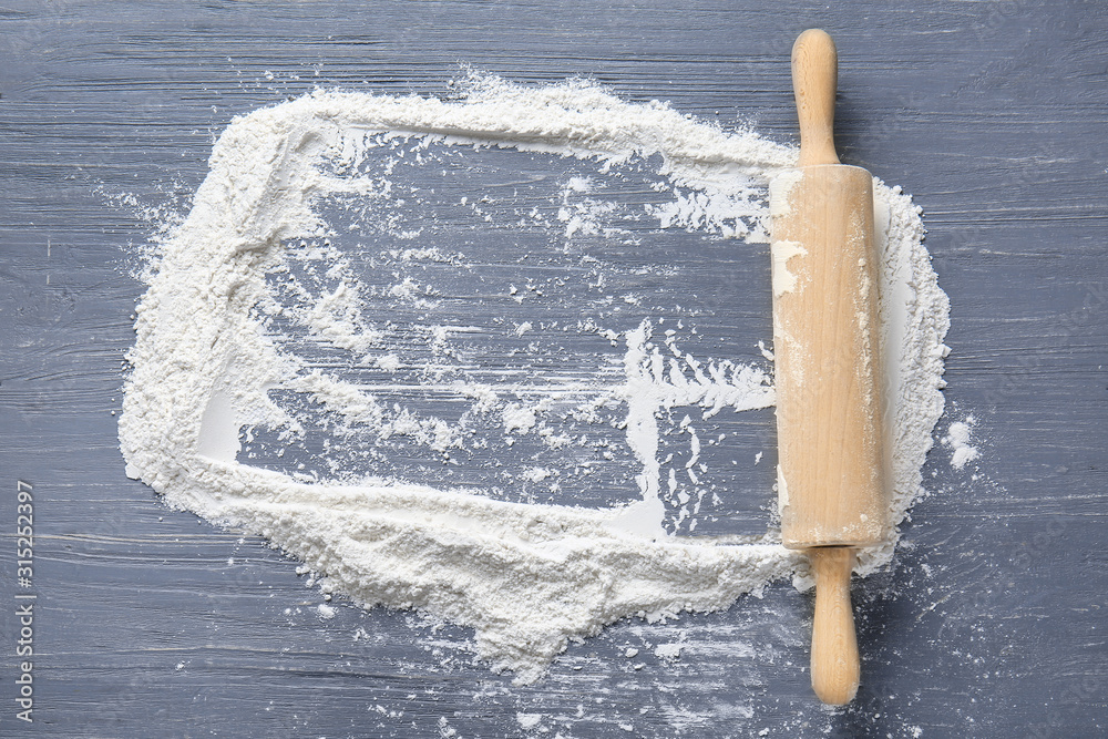Rolling pin and frame made of flour on wooden background