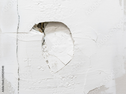 Large punched hole in wall. Close up. Recurrent drywall damage from door hitting the wall. Spackling compound applied with new damage visible. Aggressive and violent.