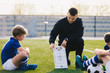 © matimix - Young Soccer Trainer Coach Explaining Tactic on Team Sports Tactics Board. Children During Soccer Football Coaching Session. Boys in Soccer Team Listening to Coach