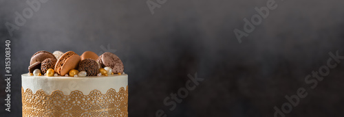 Confectionery, bakery banner. Festive cake decorated with chocolate candies and macaroons on dark background. Copy space, close up