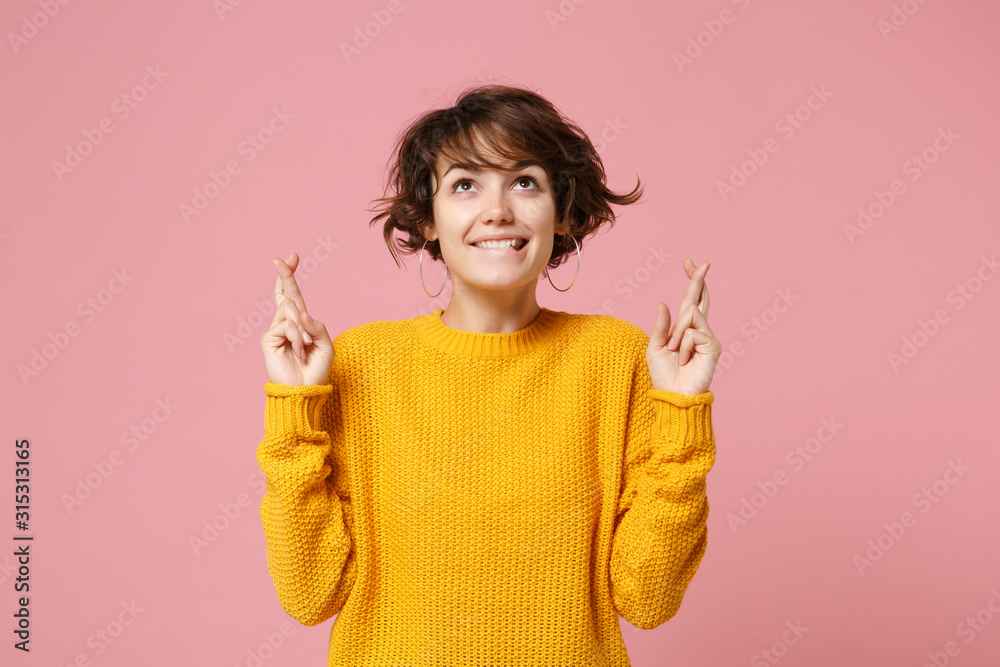 Pretty young brunette woman in yellow sweater posing isolated on pastel pink background. People lifestyle concept. Mock up copy space. Waiting for special moment, keeping fingers crossed, making wish. - obrazy, fototapety, plakaty 