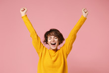 Happy Young Brunette Woman Girl In Yellow Sweater Posing Isolated On Pastel Pink Background Studio Portrait. People Lifestyle Concept. Mock Up Copy Space. Doing Winner Gesture, Keeping Eyes Closed.
