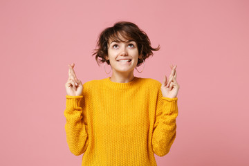 Wall Mural - Pretty young brunette woman in yellow sweater posing isolated on pastel pink background. People lifestyle concept. Mock up copy space. Waiting for special moment, keeping fingers crossed, making wish.