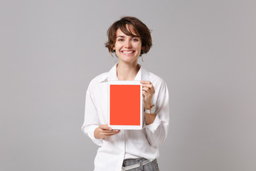 Wall Mural - Funny young business woman in white shirt posing isolated on grey wall background. Achievement career wealth business concept. Mock up copy space. Holding tablet pc computer with blank empty screen.