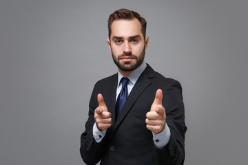 Wall Mural - Handsome young business man in classic black suit shirt tie posing isolated on grey background in studio. Achievement career wealth business concept. Mock up copy space. Point index fingers on camera.