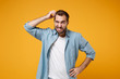 Preoccupied young bearded man in casual blue shirt posing isolated on yellow orange background studio portrait. People emotions lifestyle concept. Mock up copy space. Putting hand on head, looking up.