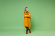 © ViDi Studio - Smiling little blonde kid girl 12-13 years old in yellow coat posing isolated on pastel green wall background children portrait. Childhood lifestyle concept. Mock up copy space. Holding hands crossed.