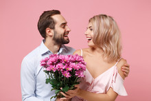 Funny Young Couple Two Guy Girl In Party Outfit Celebrating Isolated On Pastel Pink Background. Valentine's Day Women's Day Birthday Holiday Concept. Holding Bouquet Of Flowers, Looking At Each Other.