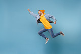 Fototapeta  - Side view of young hipster guy in fashion jeans denim clothes posing isolated on pastel blue background. People lifestyle concept. Mock up copy space. Jumping with outstretched hand like Superman.