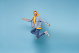 Fototapeta  - Side view of funny young hipster guy in fashion jeans denim clothes posing isolated on pastel blue background. People lifestyle concept. Mock up copy space. Jumping, spreading hands, looking aside.