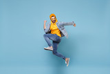 Fototapeta  - Side view of happy young hipster guy in fashion jeans denim clothes posing isolated on pastel blue background studio portrait. People lifestyle concept. Mock up copy space. Jump doing winner gesture.
