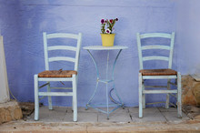 Wooden Two Chairs And Stylish Table On The Blue Background Wall In Greek Style. Outdoor Patio Cafe With Empty Sitting Place.