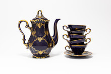Closeup Of A Beautiful Cobalt Blue Colored Vintage Porcelain Tea Set With Golden Floral Pattern On White Background. The Set Includes A Tea Pot, And A Stack Of Tea Cups.