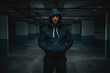 Serious attractive muscular caucasian sportsman in hoodie standing in underground garage with hands in pockets at night. Urban life concept.