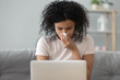 African woman holding handkerchief blowing runny nose working on laptop