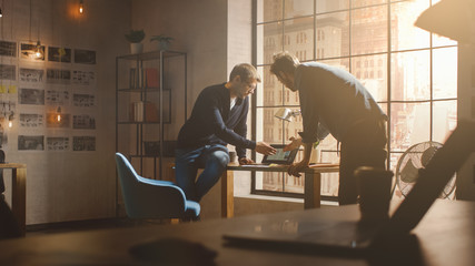 Aufkleber - Two Young and Handsome Designers Sit on the Desk and Discuss Social Media App Interfaces on Their Laptops. They Work in a Sunny Creative Office Loft with a Big Window View on Modern Urban City.