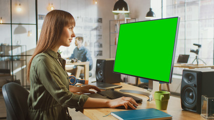 Poster - Beautiful Brunette Female Video Editor Works on Her Personal Computer with Big Green Screen Mock Up Display. She Works in a Cool Office Loft. Other Male Creative Colleague Sitting in the Background.