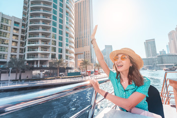 Poster - Asian girl on a boat cruise ship waving hand with skyscrapers of Marina port in Dubai