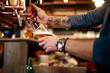 © chika_milan - Tattooed caucasian barman pouring beer while standing in pub. Selective focus on hand.