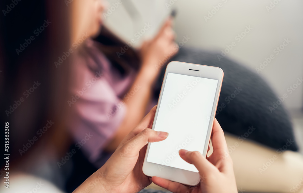 Woman hand holding smartphone with blank screen on sofa in house with friends. Take your screen to put on advertising. - obrazy, fototapety, plakaty 