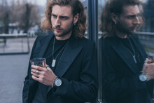 Fashionable Businessman In Black Suit Holding Glass Of Whiskey Near Office Building
