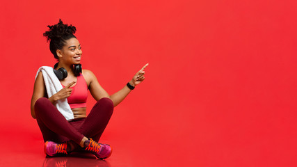 Wall Mural - Cheerful fitness model sitting on floor, pointing at free space